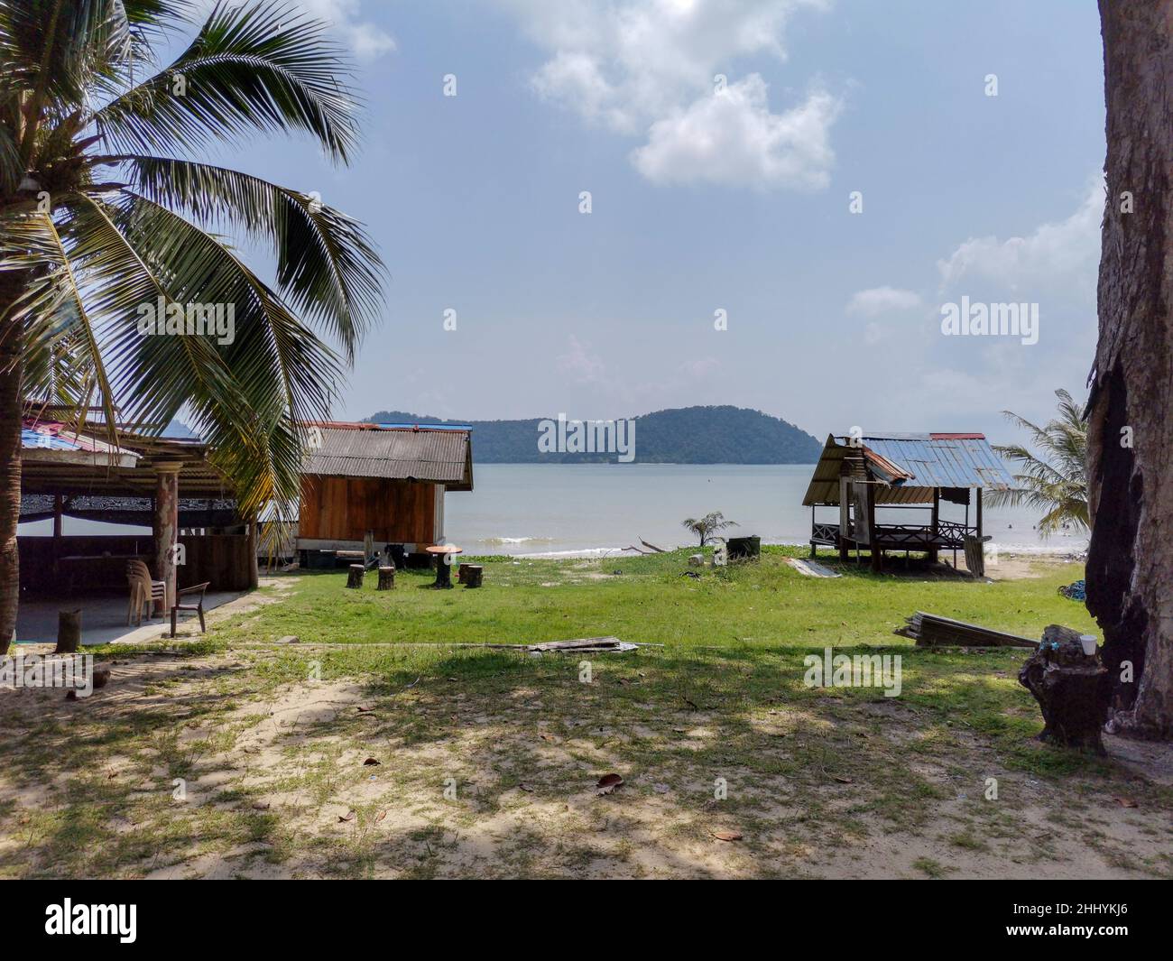 Summer wooden gazebo on a sandy beach with grass meadow, blue sky, sea wave, palm tree in the background. Tropical beach. Beautiful coast. Country hol Stock Photo