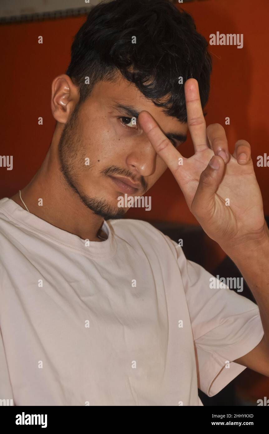 Close-up shot of a handsome young men showing peace sign with his hand, sitting indoors with looking at camera Stock Photo
