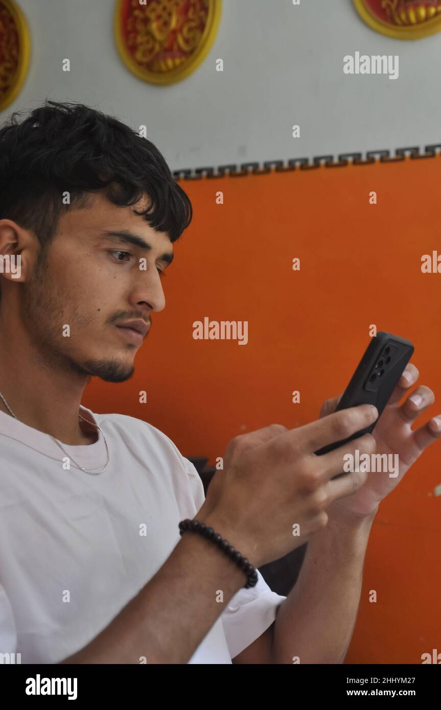 Side view of a good looking young men using phone while sitting indoors Stock Photo