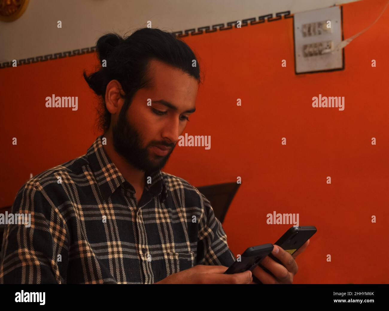 Close-up side view of a handsome bearded man with hair bun, holding two phones - Stock Photo Stock Photo