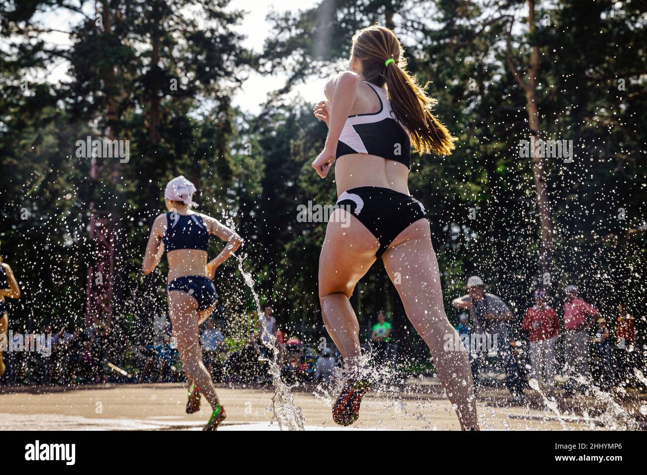 young female athlete run steeplechase in splashing water Stock Photo