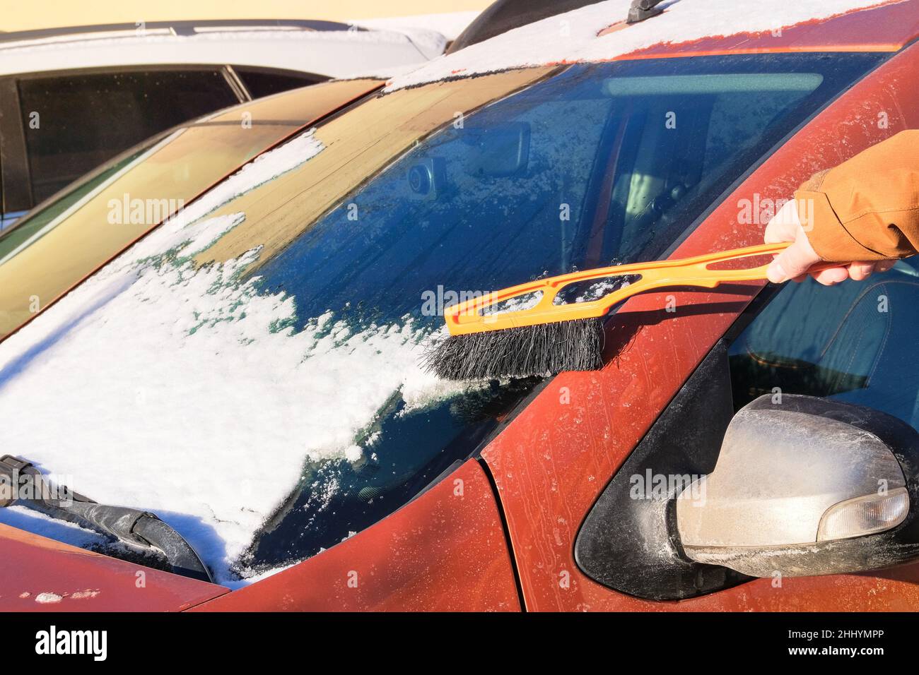 Remove lot of snow from  auto. Brush in mans hand. Man clears orange car from snow. Windshield of car. Stock Photo