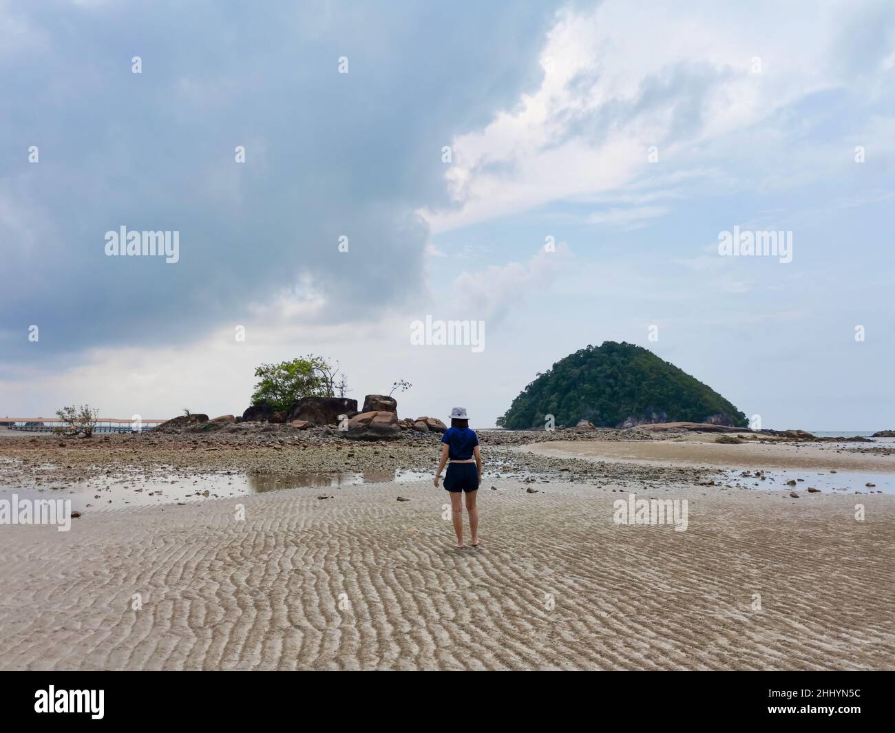 Happy girl traveler on beach at low tide with small island and rock mountain and cloudy sky background. Freedom and happiness concept. Travel lifestyl Stock Photo