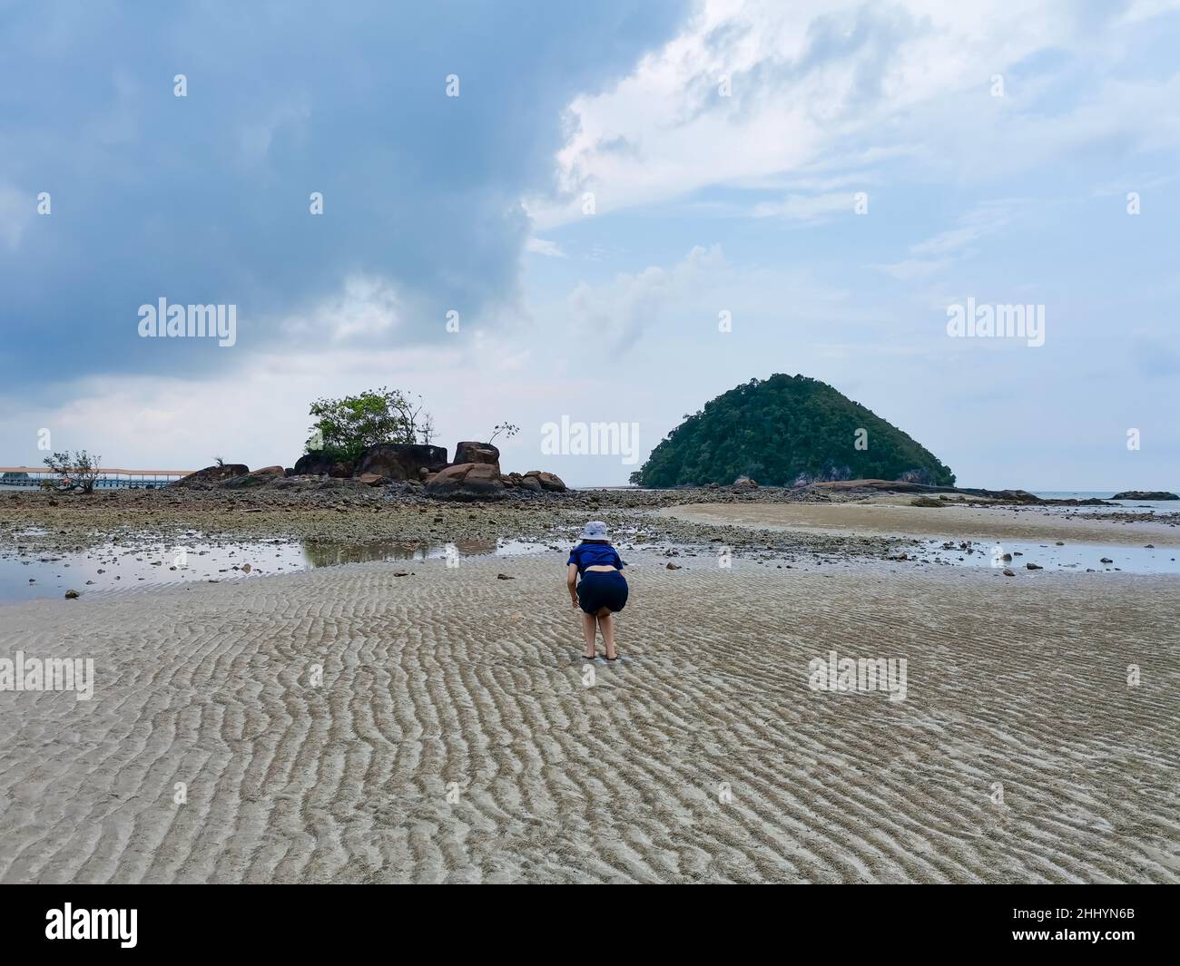 Happy girl traveler on beach at low tide with small island and rock mountain and cloudy sky background. Freedom and happiness concept. Travel lifestyl Stock Photo