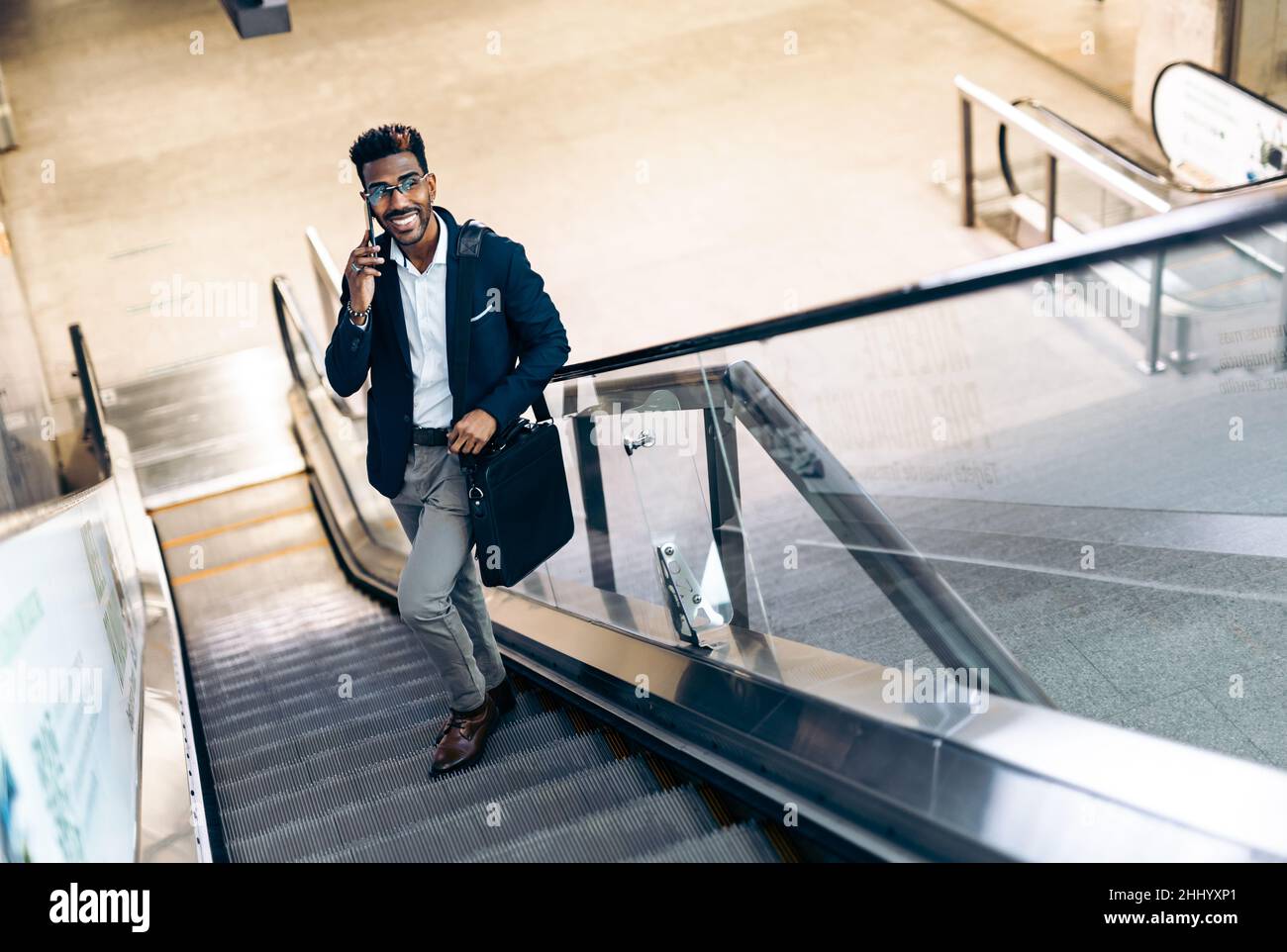 Smiling young black businessman using his smartphone on an escalator Stock Photo