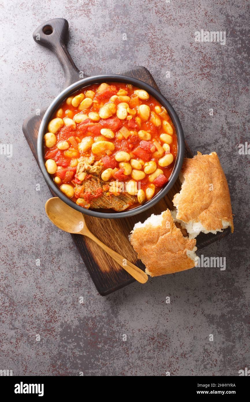 Loubia is a Moroccan dish it is a white bean stew made with tomatoes, garlic, spices like cumin closeup in the bowl on the wooden board. Vertical top Stock Photo