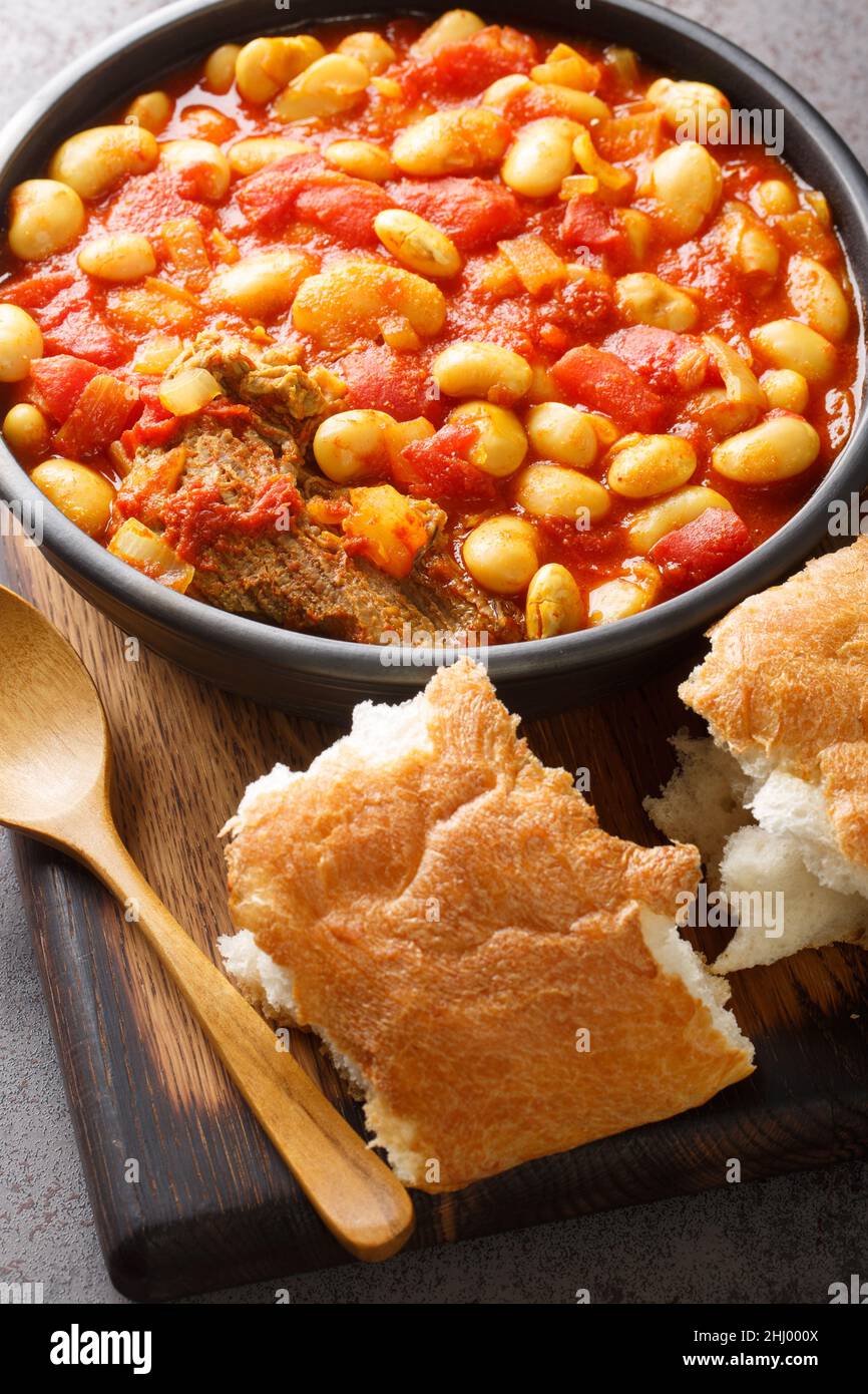 Loubia is a Moroccan dish it is a white bean stew made with tomatoes, garlic, spices like cumin closeup in the bowl on the wooden board. Vertical Stock Photo