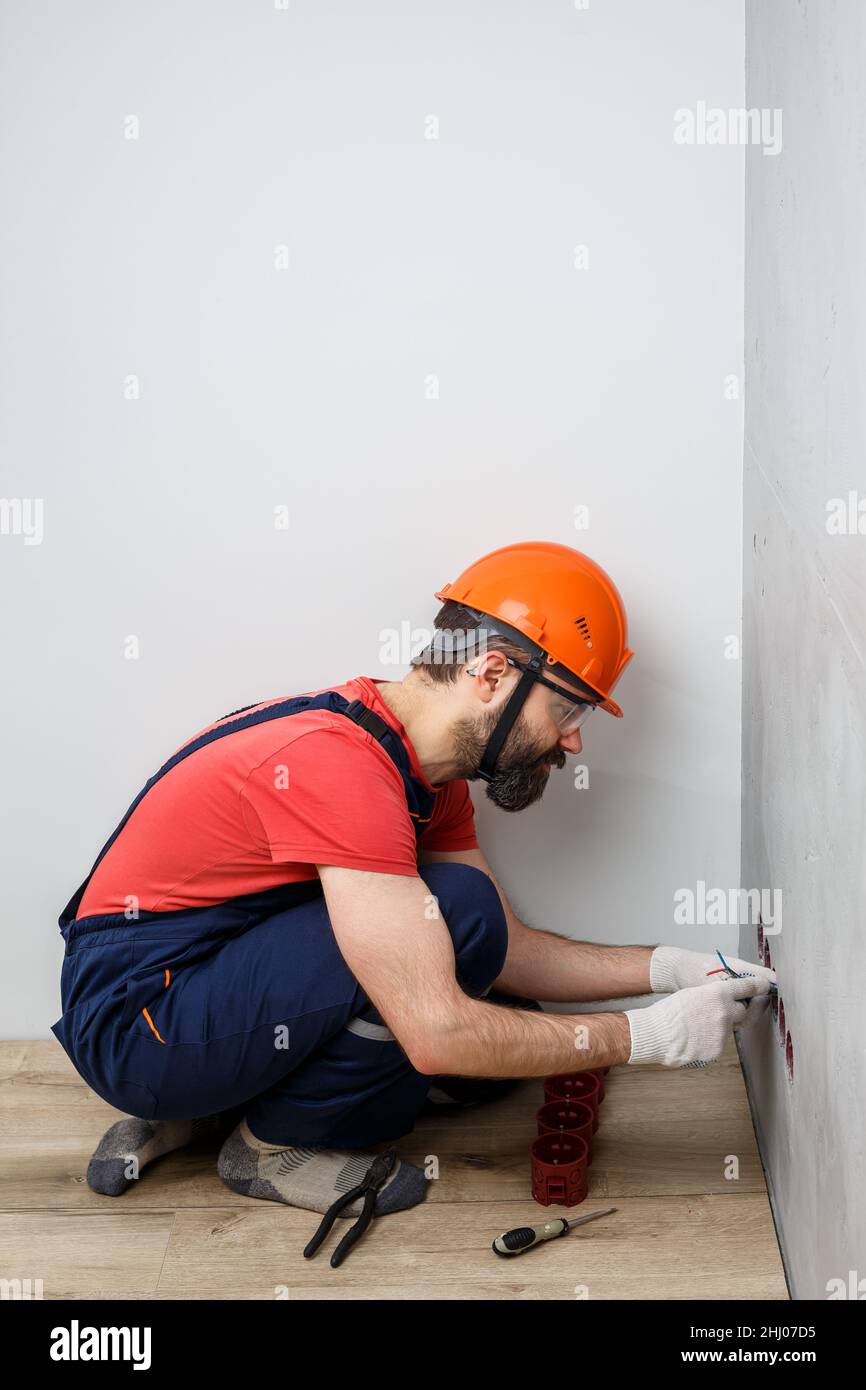 electrician in helmet installs sockets Stock Photo