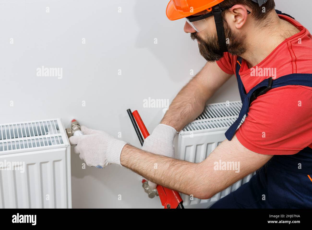 a worker in an orange helmet installs radiators in the house Stock Photo