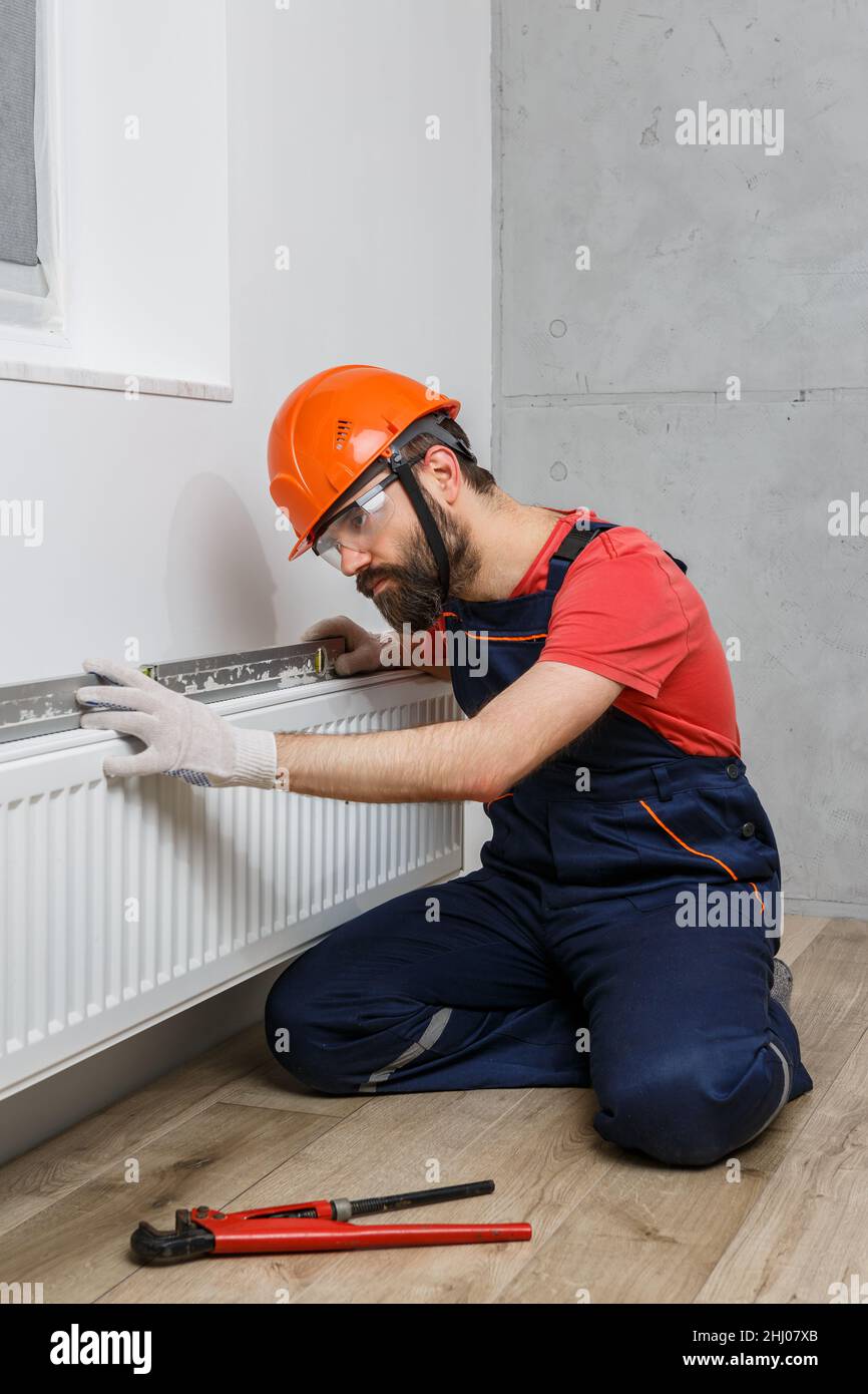 a worker in an orange helmet installs radiators in the house Stock Photo