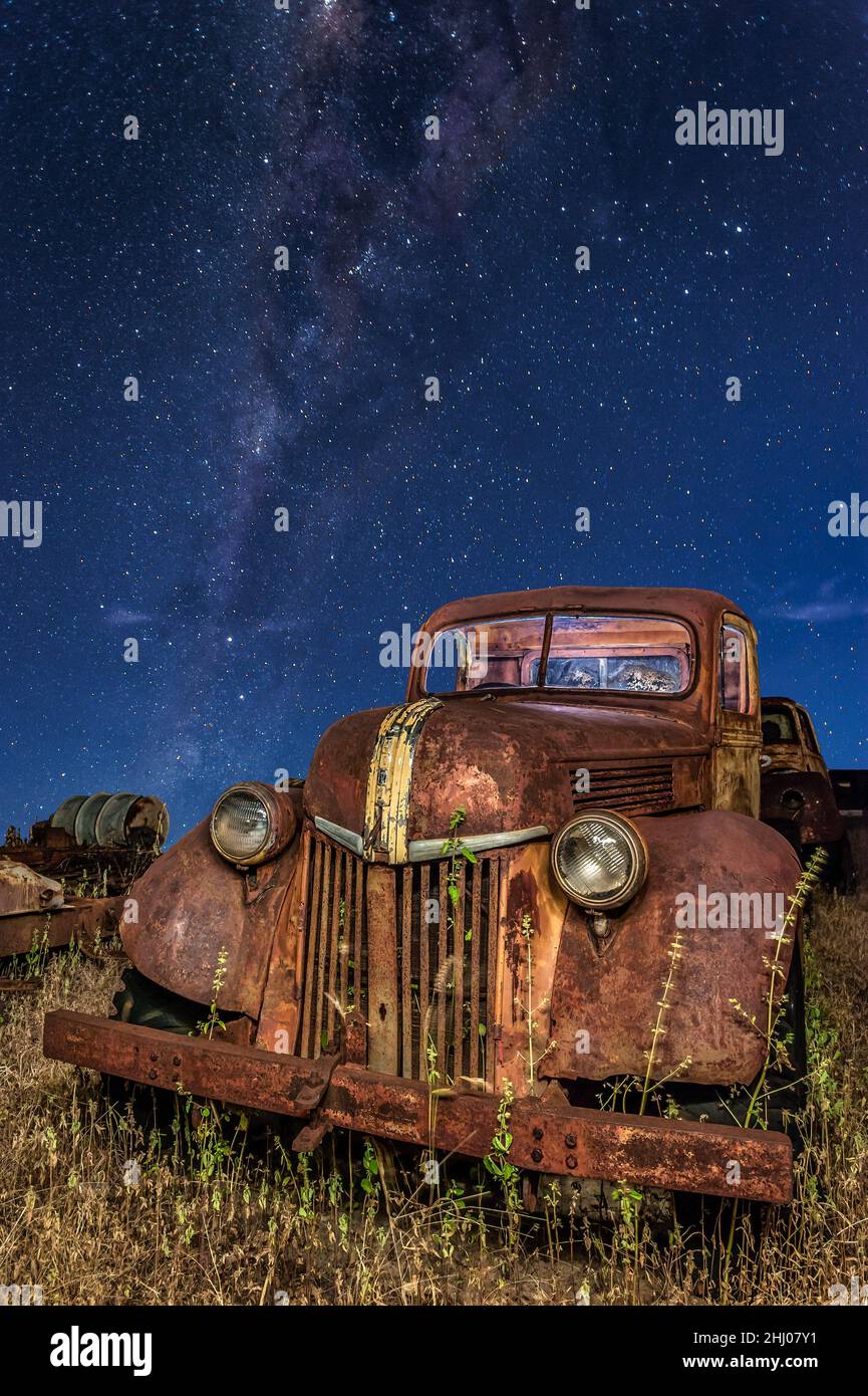 An old, abandoned, vintage ford pick-up lying in a grassy field on a Chillagoe property in Queensland with the milkyway core in the background. Stock Photo