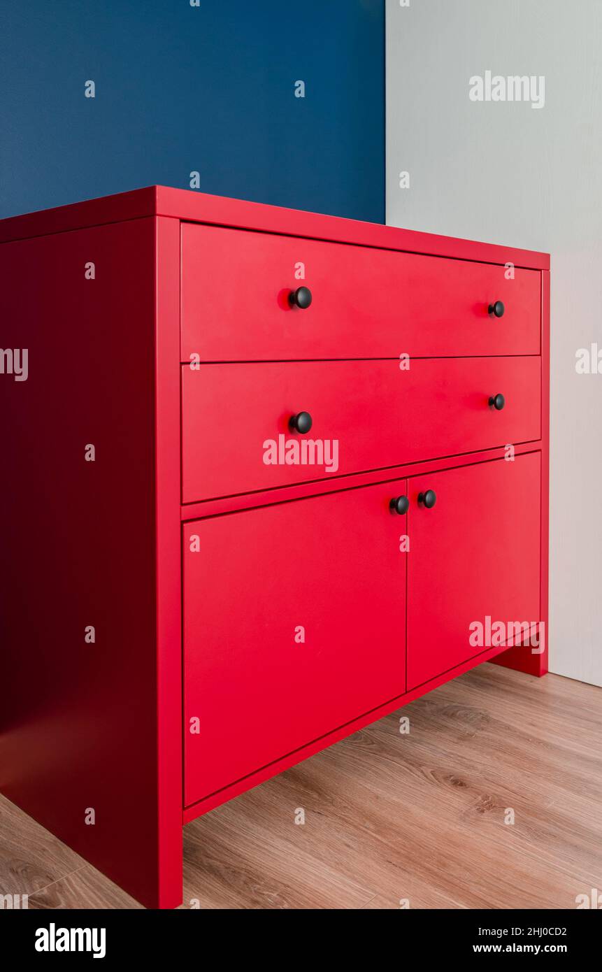 Red chest of drawers in a Scandinavian interior. A red wooden cabinet with  black handles stands in an apartment against a blue wall next to a white wa  Stock Photo - Alamy