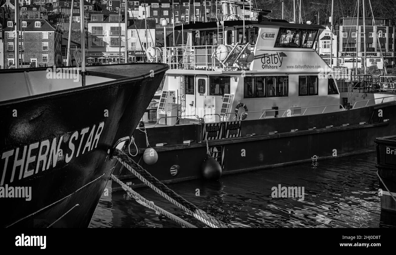 The harbour at Scarborough.  An offshore supply vessel is moored in harbour with the bow of a boat in the foreground.  Buildings are in the background Stock Photo