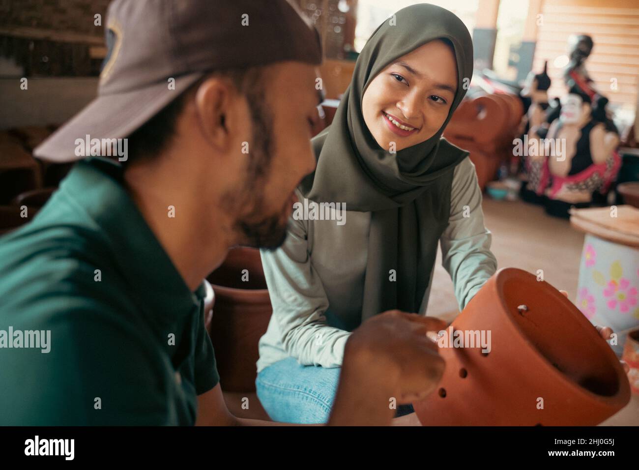 veiled woman observing pottery craft with young man Stock Photo