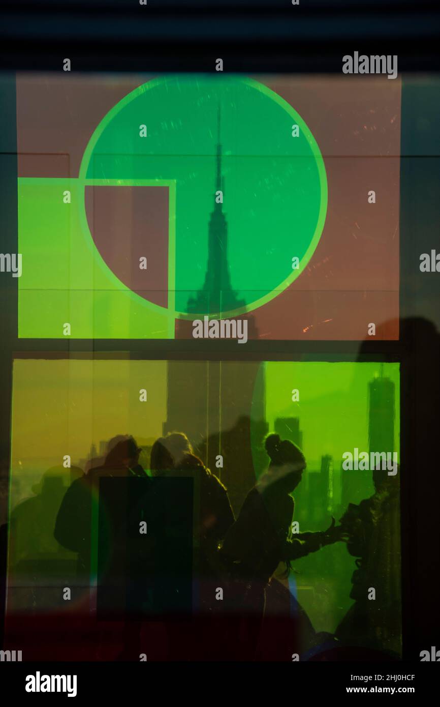 Buntes Treiben auf dem Rockefeller Center hinter gefärbten Scheiben und dem Blick auf die Silhouette des Empire State Buildings Stock Photo