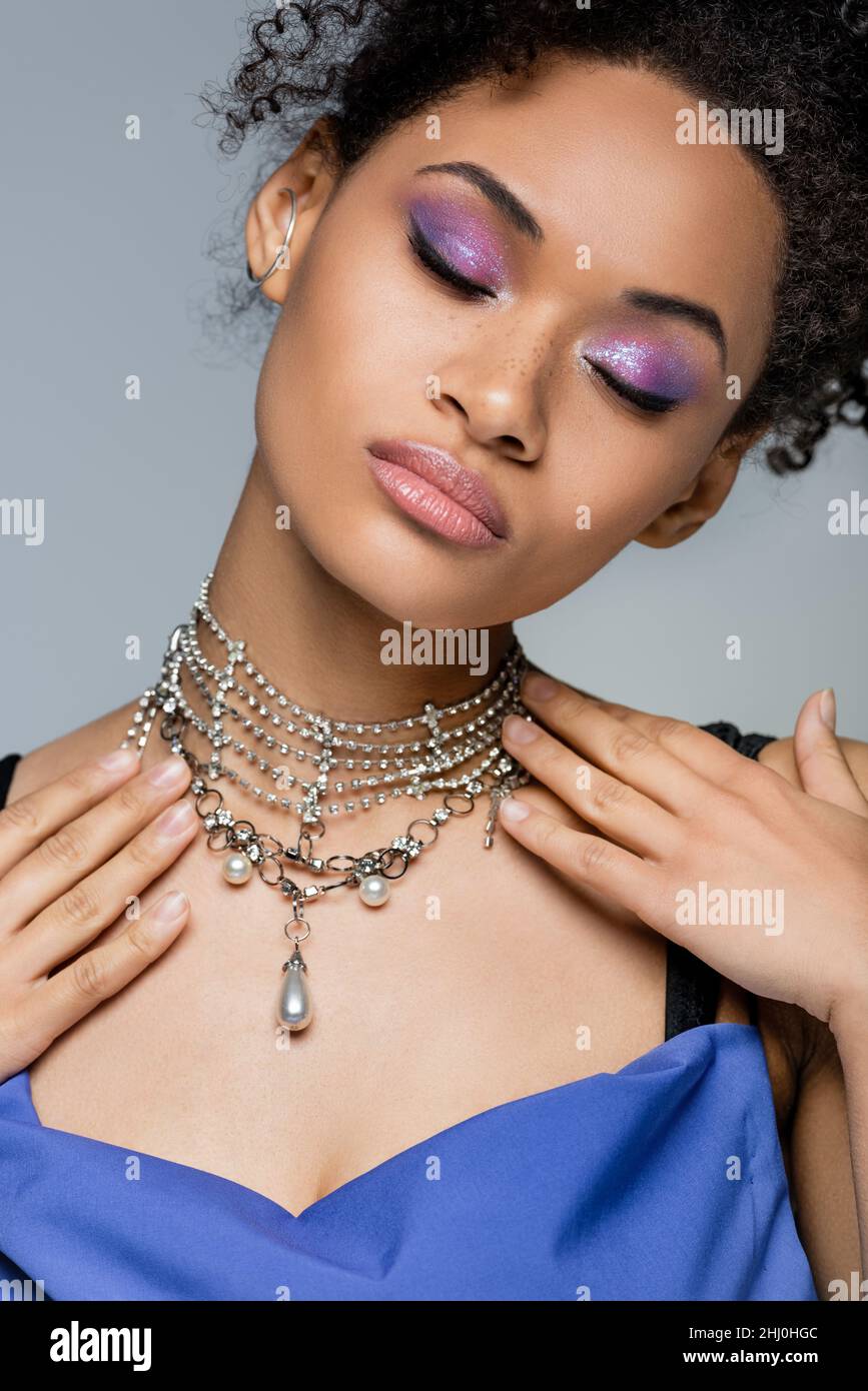 curly african american woman with purple eye shadow and closed eyes isolated on grey Stock Photo
