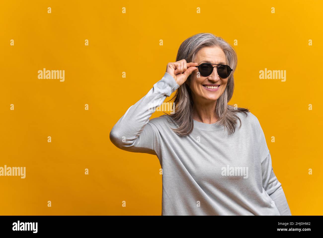 Horizontal shot of retirement female model wears stylish clothes and big sunglasses, posing cheery, buying clothes of last trends against yellow background Stock Photo