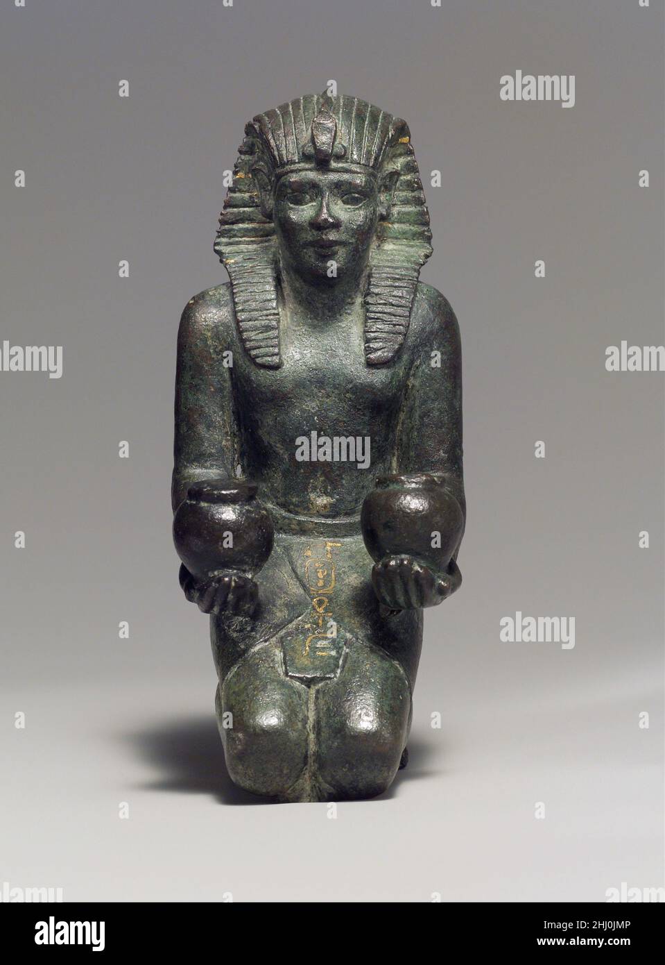 Kneeling statuette of King Amasis 570–526 B.C. Late Period, Saite The childlike appearance of this kneeling statuette, with its large head, beautiful features, plump body, and short legs, is characteristic of some metal royal statues made during the Late Period, when the king was associated with juvenile gods such as Horus, son of Isis. This work, like the stone statuary from the reign of Amasis, testifies to the high level of artistry attained during his rule.The figure is solid-the body, limbs, and attributes were all integrally cast. Precious-metal leaf once covered the king's nemes; additi Stock Photo