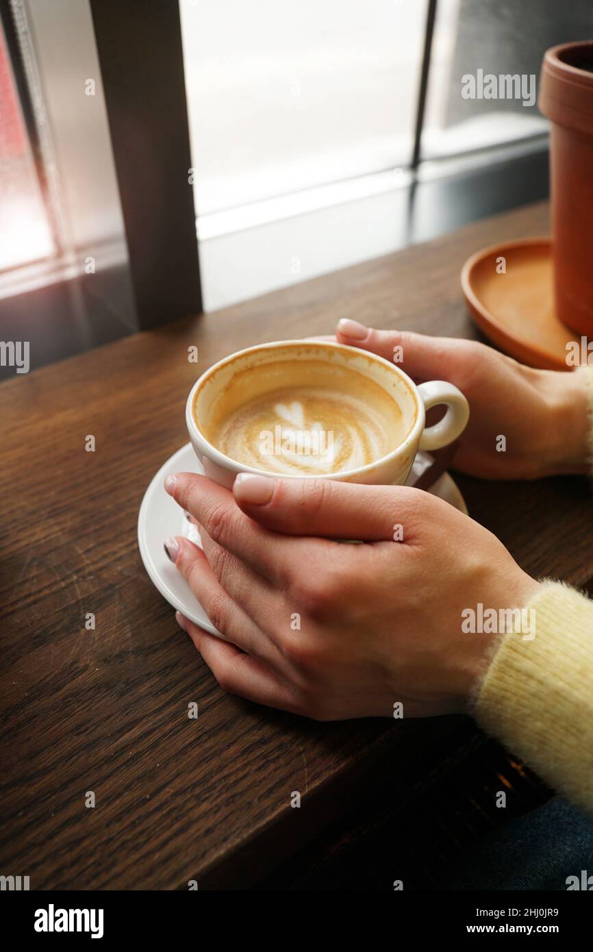 Woman hands in yellow sweater holding cup of coffee with latte art on ...