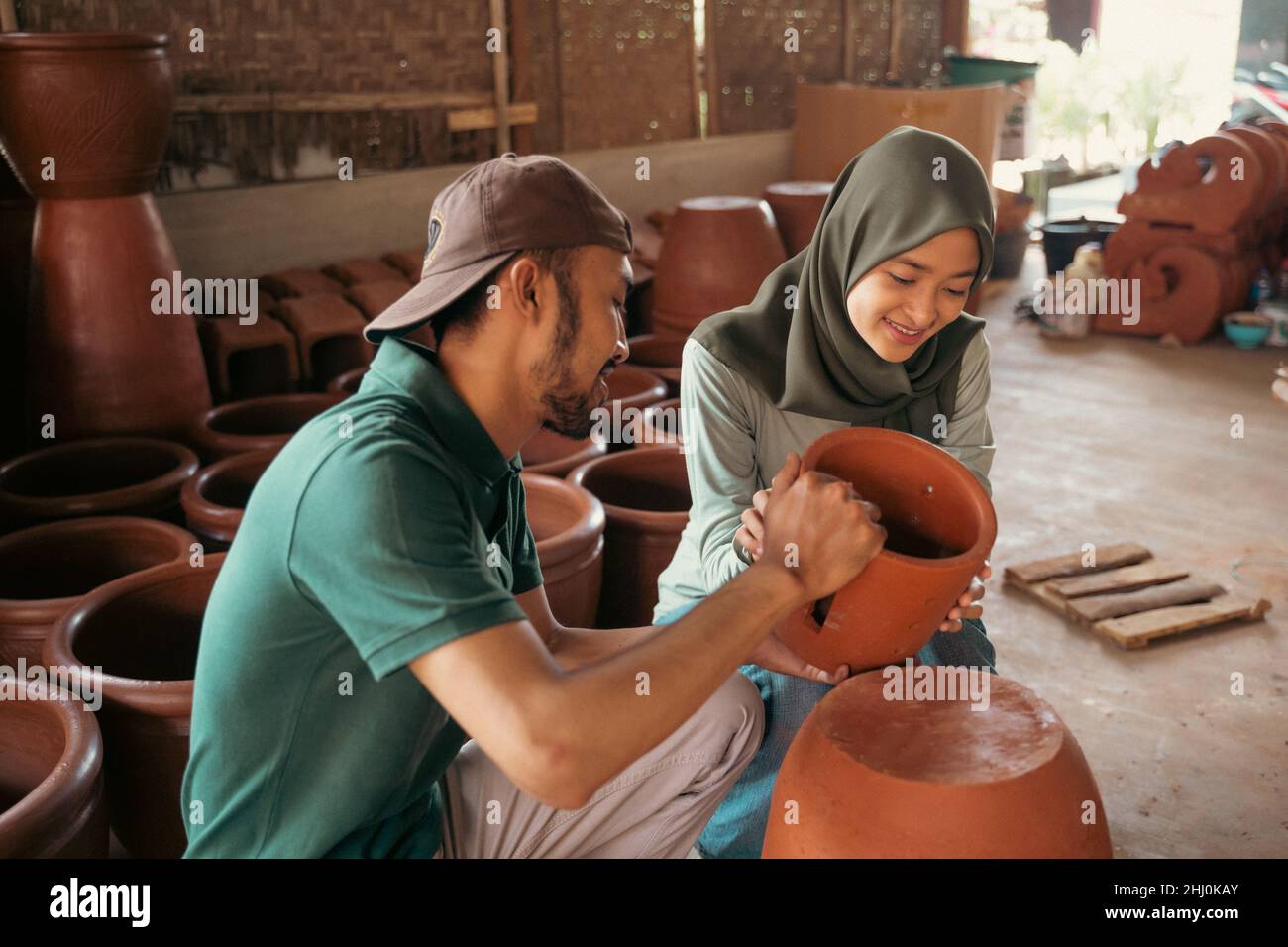 Man and girl in hijab holding pottery while chatting Stock Photo