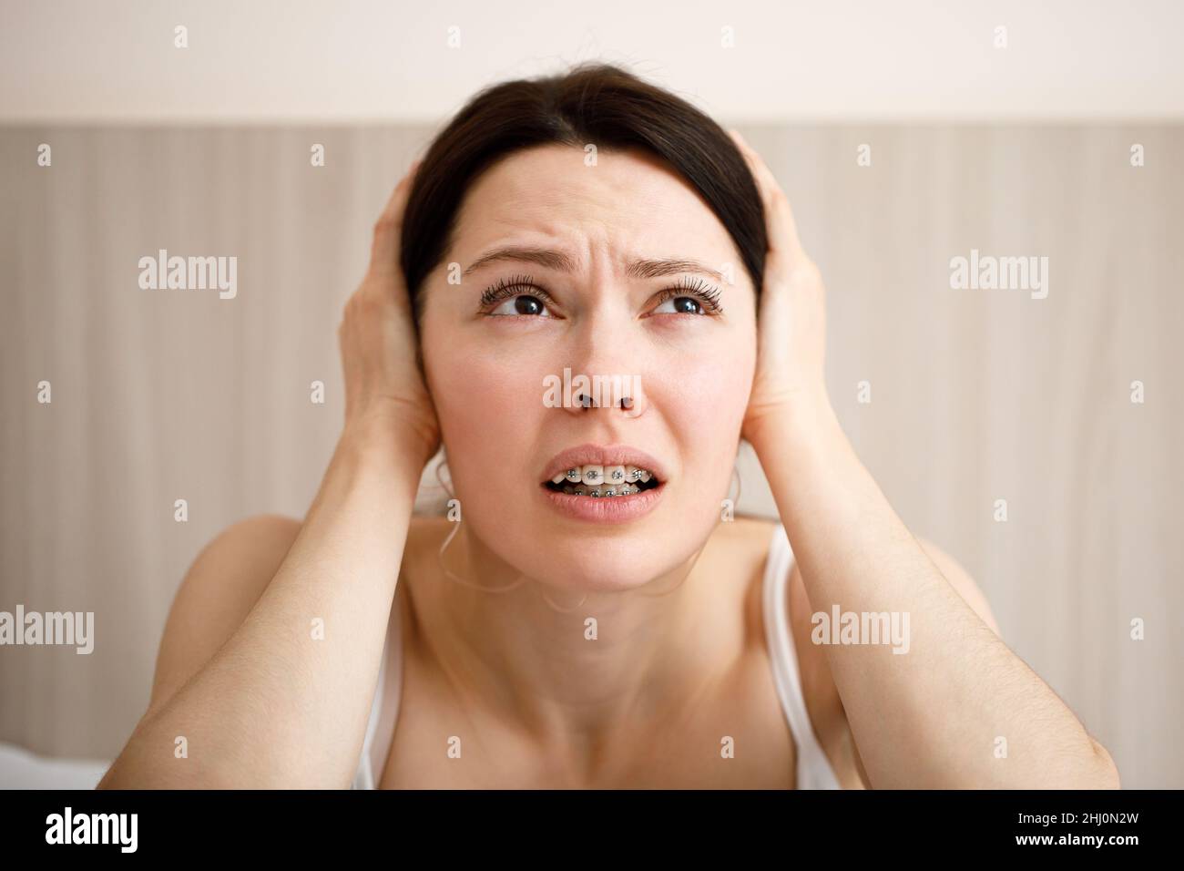The woman covers her ears because of the loud noise. Noisy neighbors listen to loud music and interfere with sleep. Using earplugs. Stock Photo