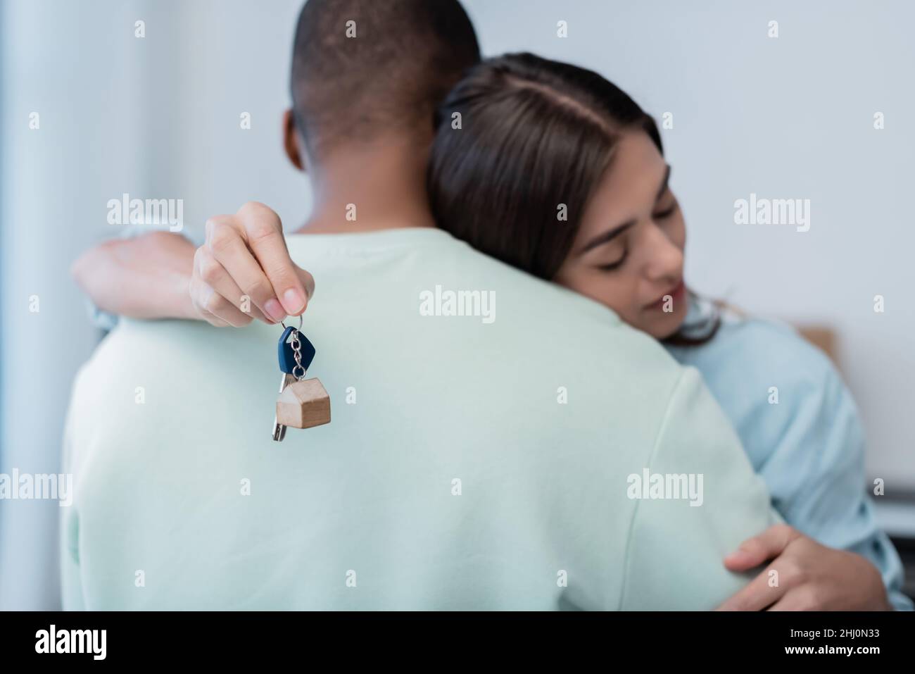 young woman holding key from new apartment and hugging african american ...