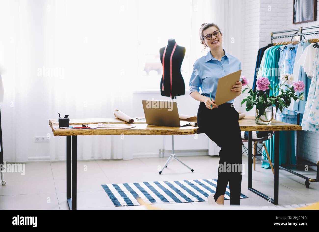 Cheerful dressmaker in creative workplace with clothes Stock Photo