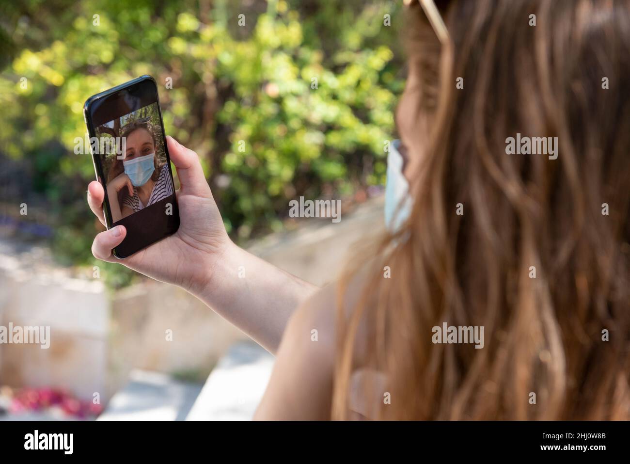 Unrecognizable woman with facial mask uses smart phone to take selfie. Stock Photo