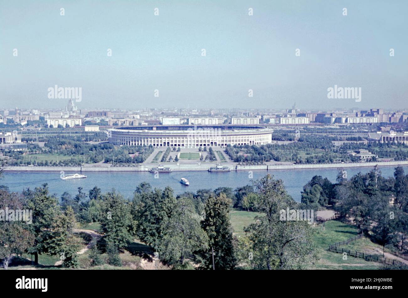 A 1960s photograph of the Luzhniki Stadium and its surroundings, located by the Moskva River, Moscow, Russia. The full name of the ‘National Stadium’ is ‘Grand Sports Arena of the Luzhniki Olympic Complex’. Its total seating capacity of 81,000 – the largest football stadium in Russia. The stadium was built in 1955–56 as the Grand Arena of the Central Lenin Stadium. The original stadium was demolished in 2013 to make way for a new stadium. However, the self-supported roof (built in1996) and the original facade wall were retained – a vintage 1960s photograph from an amateur colour transparency. Stock Photo