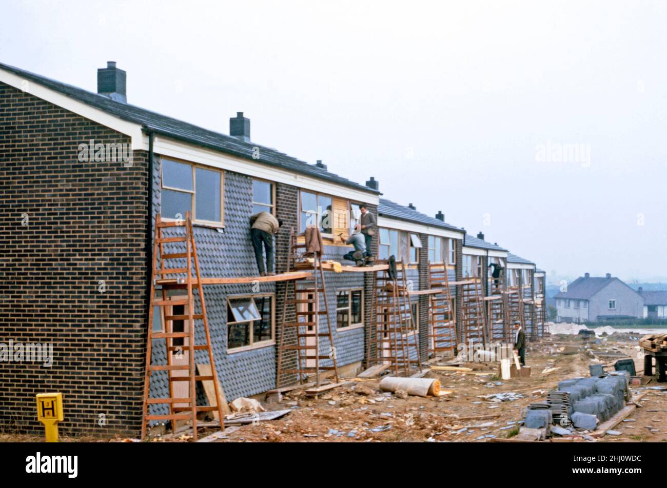 Modern house construction in Stevenage New Town, Hertfordshire, England, UK in 1963. Here, on the fronts of a terrace of houses, a hung-tile finishing layer being applied – see Alamy 2HJ0WGN for a view of the insulation and battens below the outer layer. The work seems slightly dangerous – health and safety regulations would require extensive scaffolding and hard hats being worn today. Stevenage lies about 30 miles (50 km) north of London. In 1946 Stevenage was designated the United Kingdom's first New Town under the New Towns Act – a vintage 1960s photograph. Stock Photo