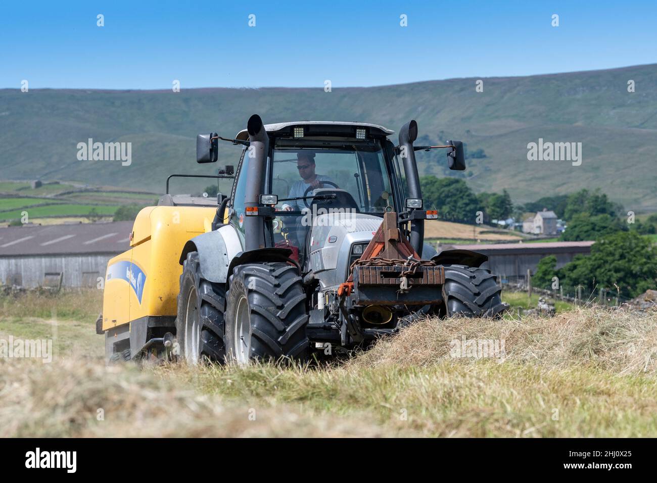 Farmer making traditional upland meadow hay, with a Hurlimann XL tractor and a New Holland BB9060 high density square baler. Hawes, North Yorkshire, U Stock Photo