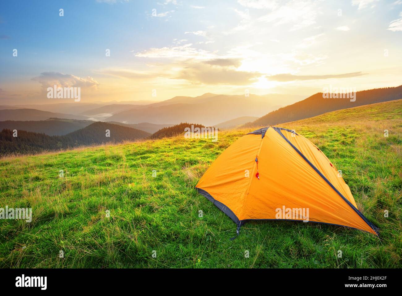 Orange tourist tent in the mountains on a meadow with green grass Stock Photo