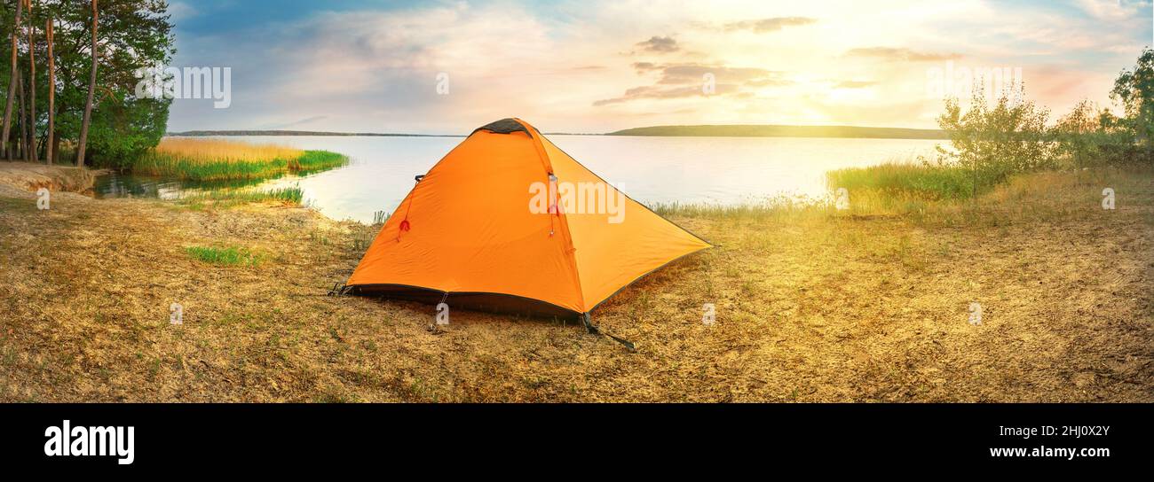 Orange tourist tent on sandy shore of lake at sunset Stock Photo