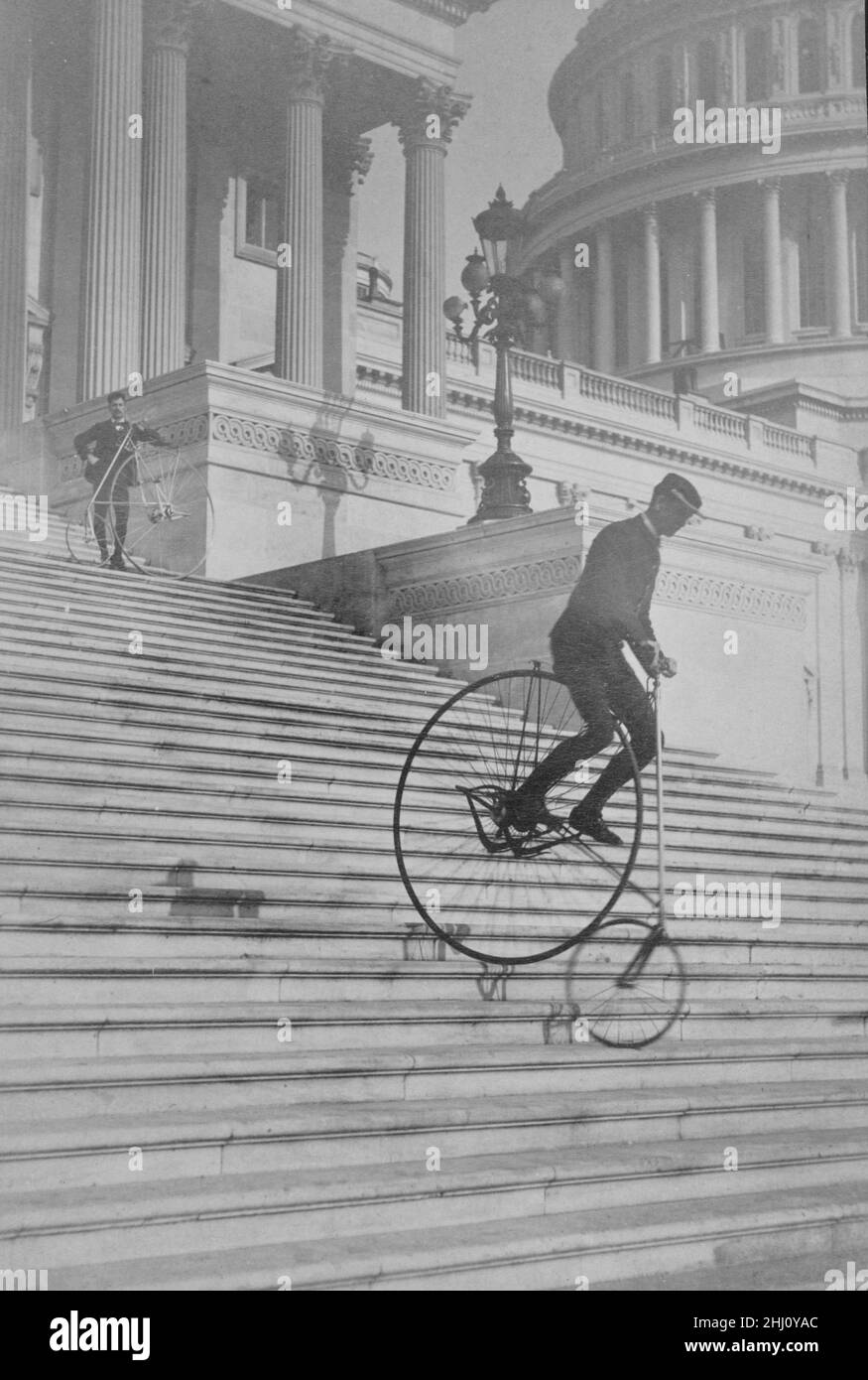 A Perilous Ride - a man rides a bicycle down the steps of the U.S. Capitol as another man with a bicycle waits at the top - Platt Brothers. Stock Photo