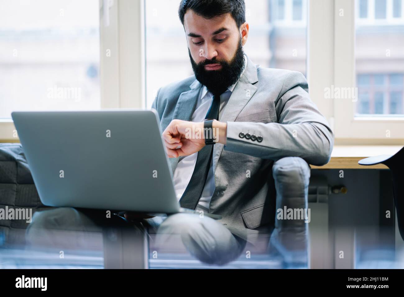Responsible businessman with laptop looking at watch Stock Photo
