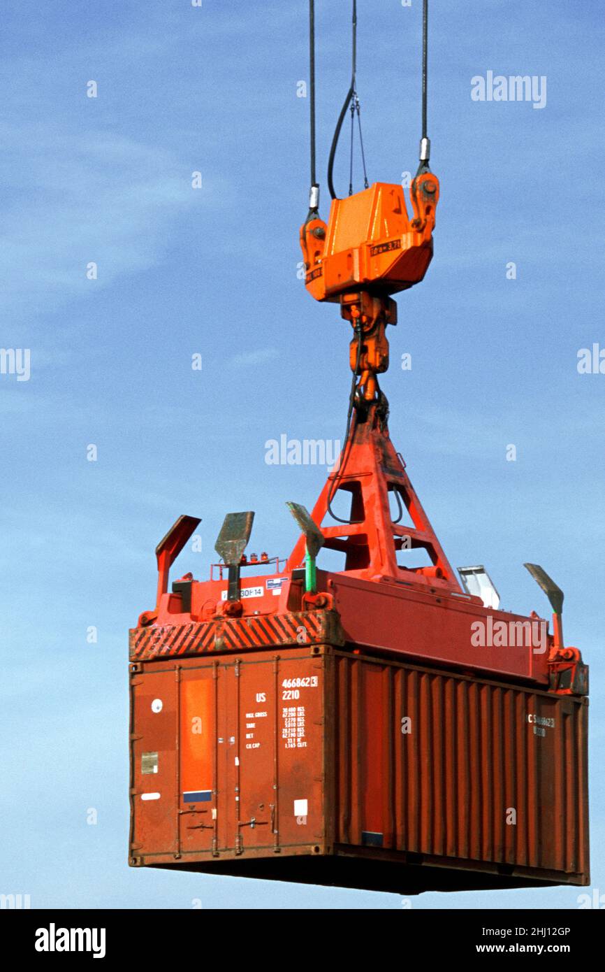 Shipping container suspended mid-air by loading crane. Cargo containers moved on industrial commercial dock. Shipping industry and commerce USA Stock Photo