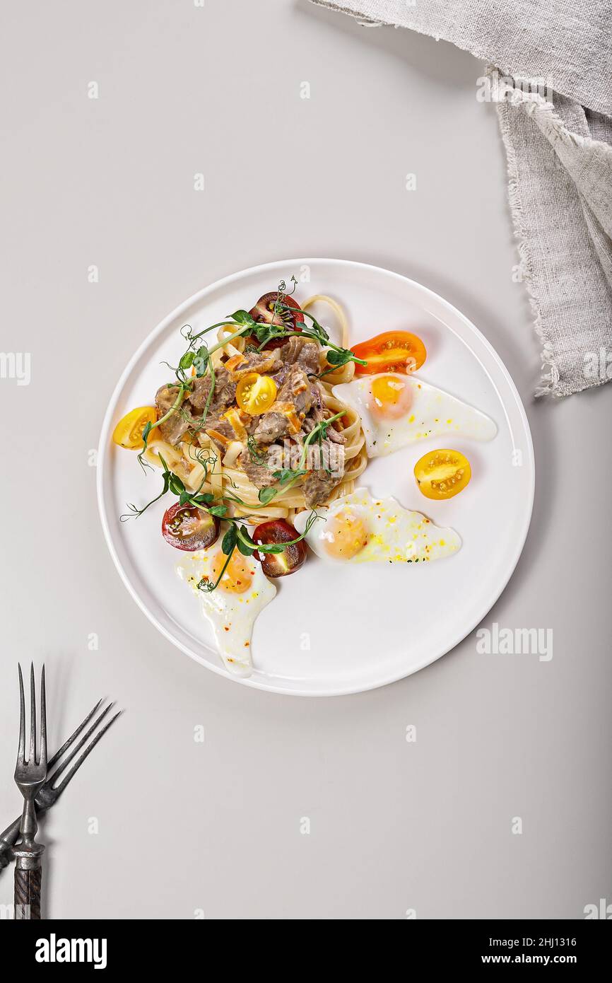 Pasta with stewed turkey, cherry tomatoes and fresh herbs. Fried quail eggs. Delicious and healthy Mediterranean cuisine recipes. Top view. Vertical s Stock Photo