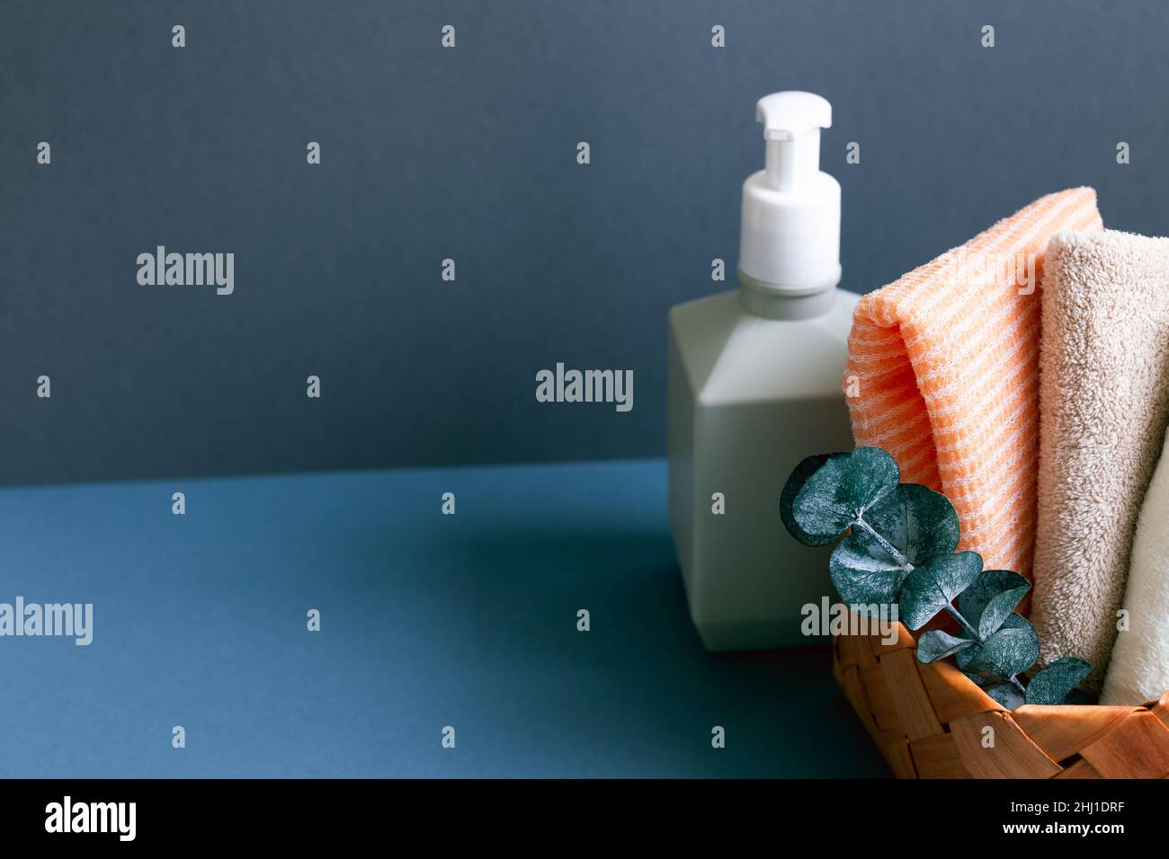 Soap dispenser and bathroom towel in basket on table. navy blue wall