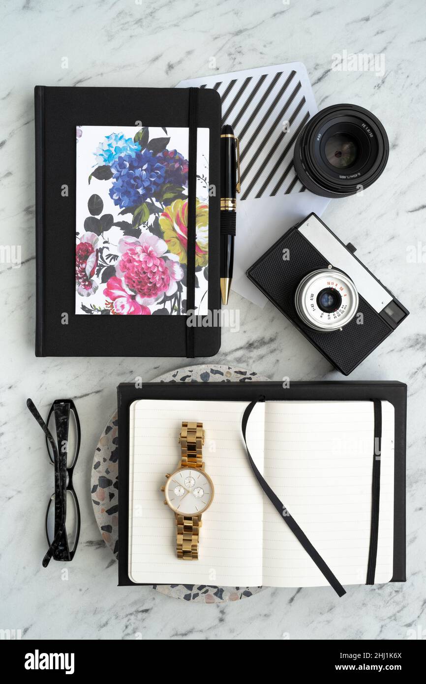 Bright and stylish blogger workplace. White marble desk with notebook, camera, lens, glasses, wristwatch, glasses and pen Stock Photo