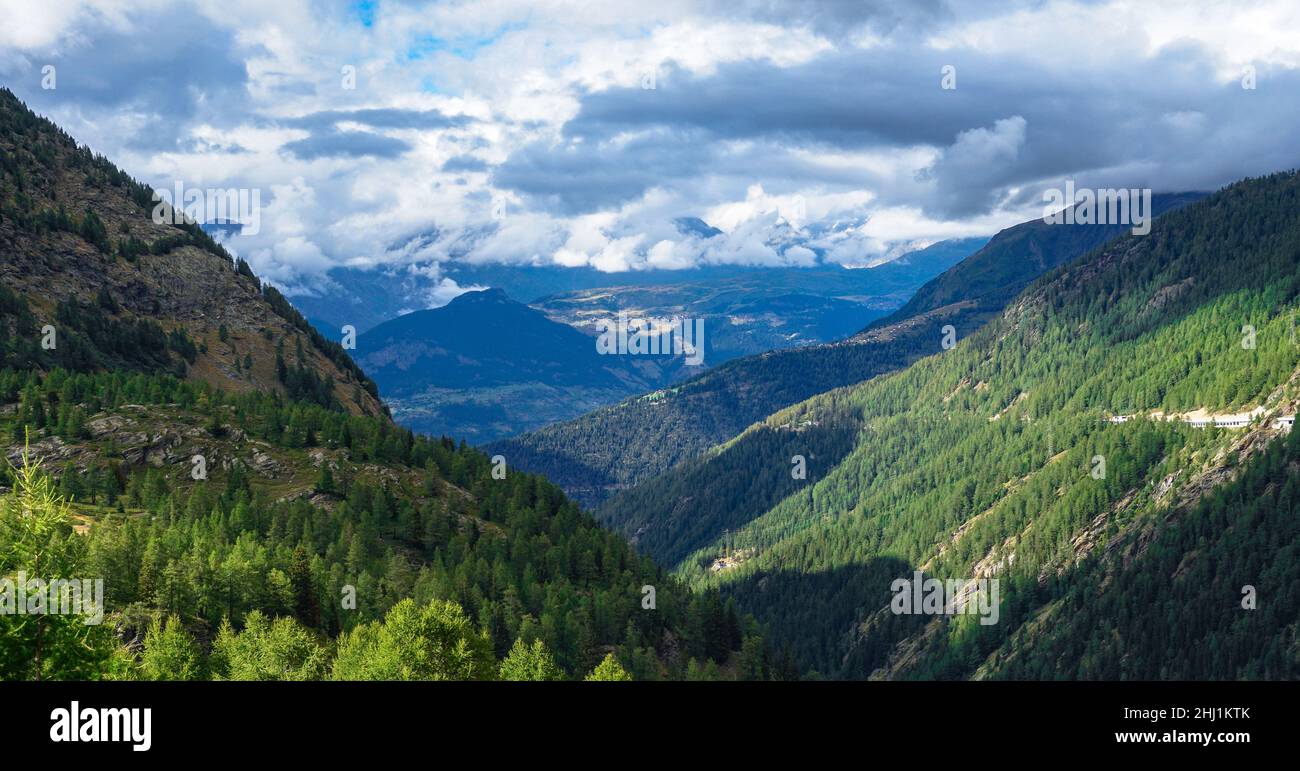 View of the Swiss Alps surrounded by forest and cumulus clouds Stock Photo