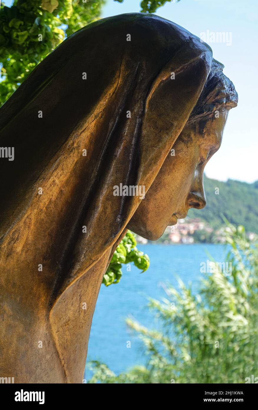Brass statue, head of a young woman in a headscarf against the background of a summer landscape Stock Photo