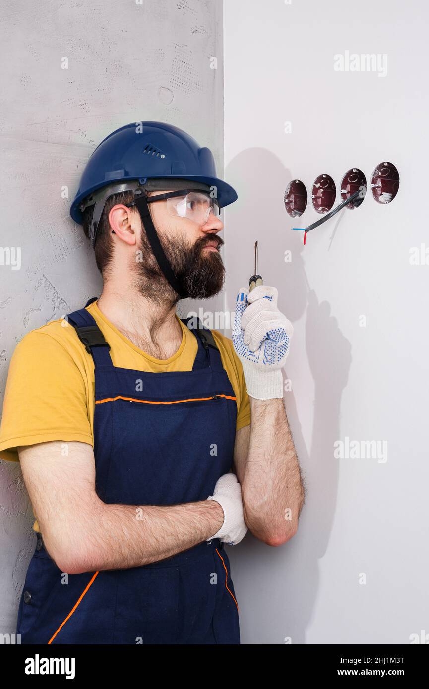 electrician in helmet installs sockets Stock Photo