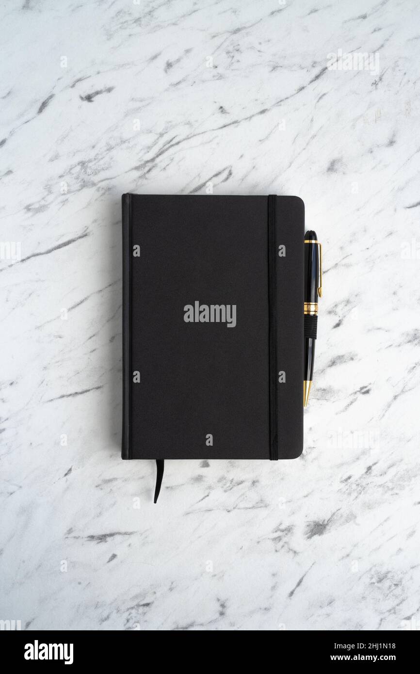 Black notebook with a pen on a marble table, top view Stock Photo