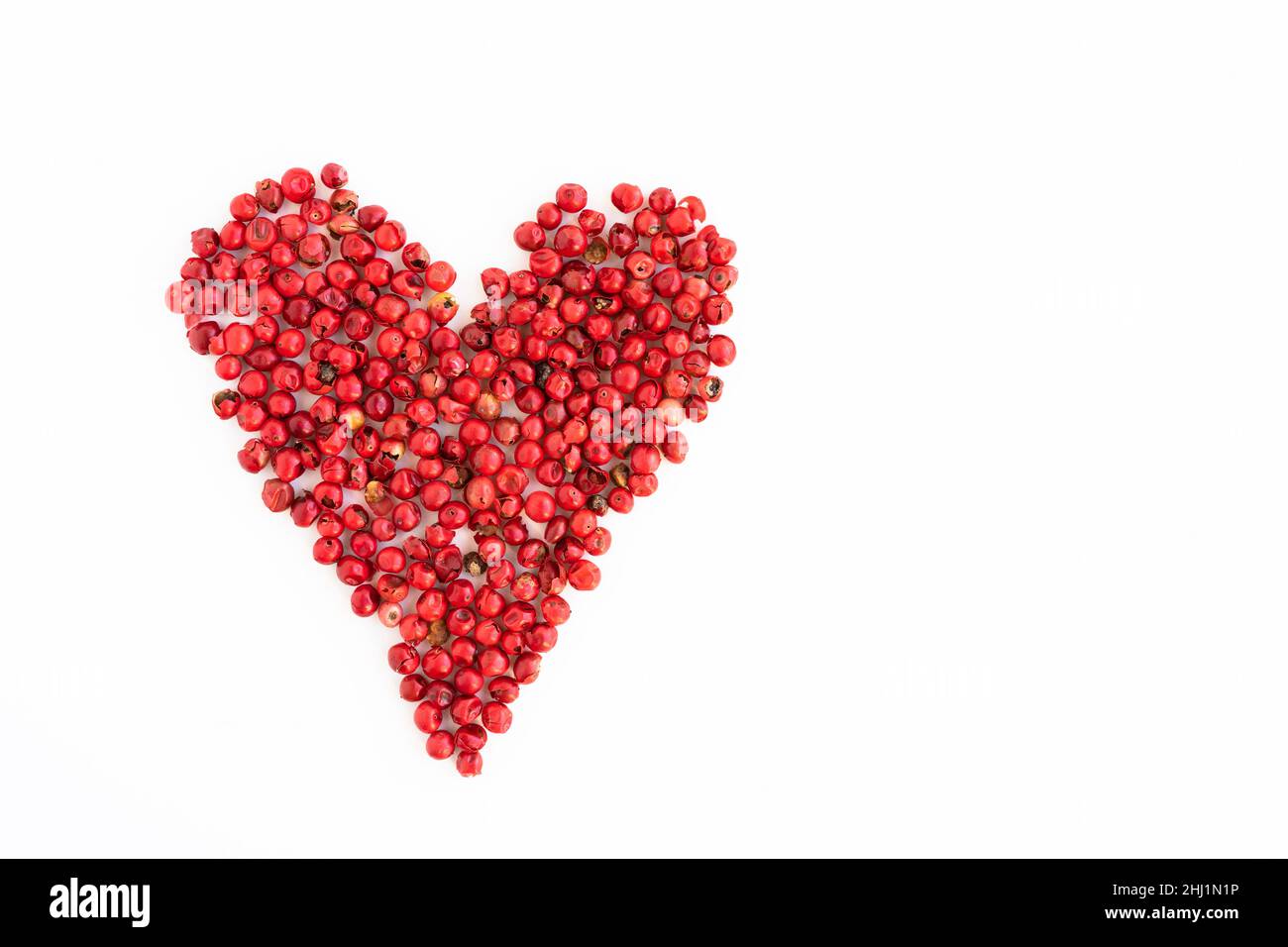 Isolated pink pepper in the shape of a heart on a white background, love of cooking Stock Photo