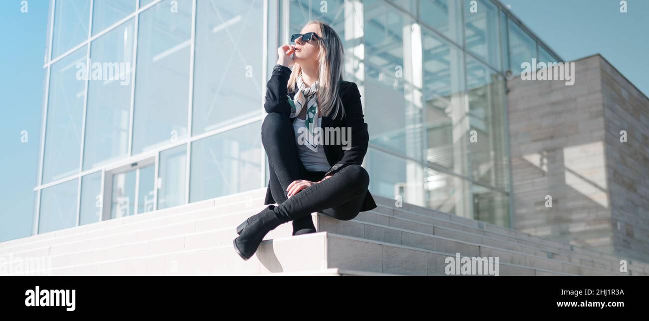 Young businesswoman sitting and thinking outside corporate building Stock Photo