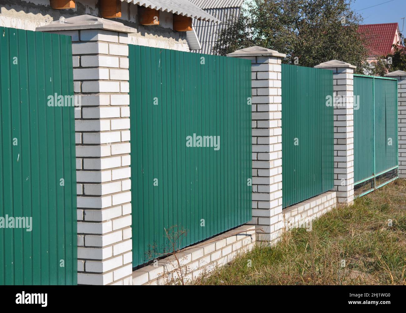 Green Metal Gate Fence with white bricks. Steel sheets fence. Stock Photo