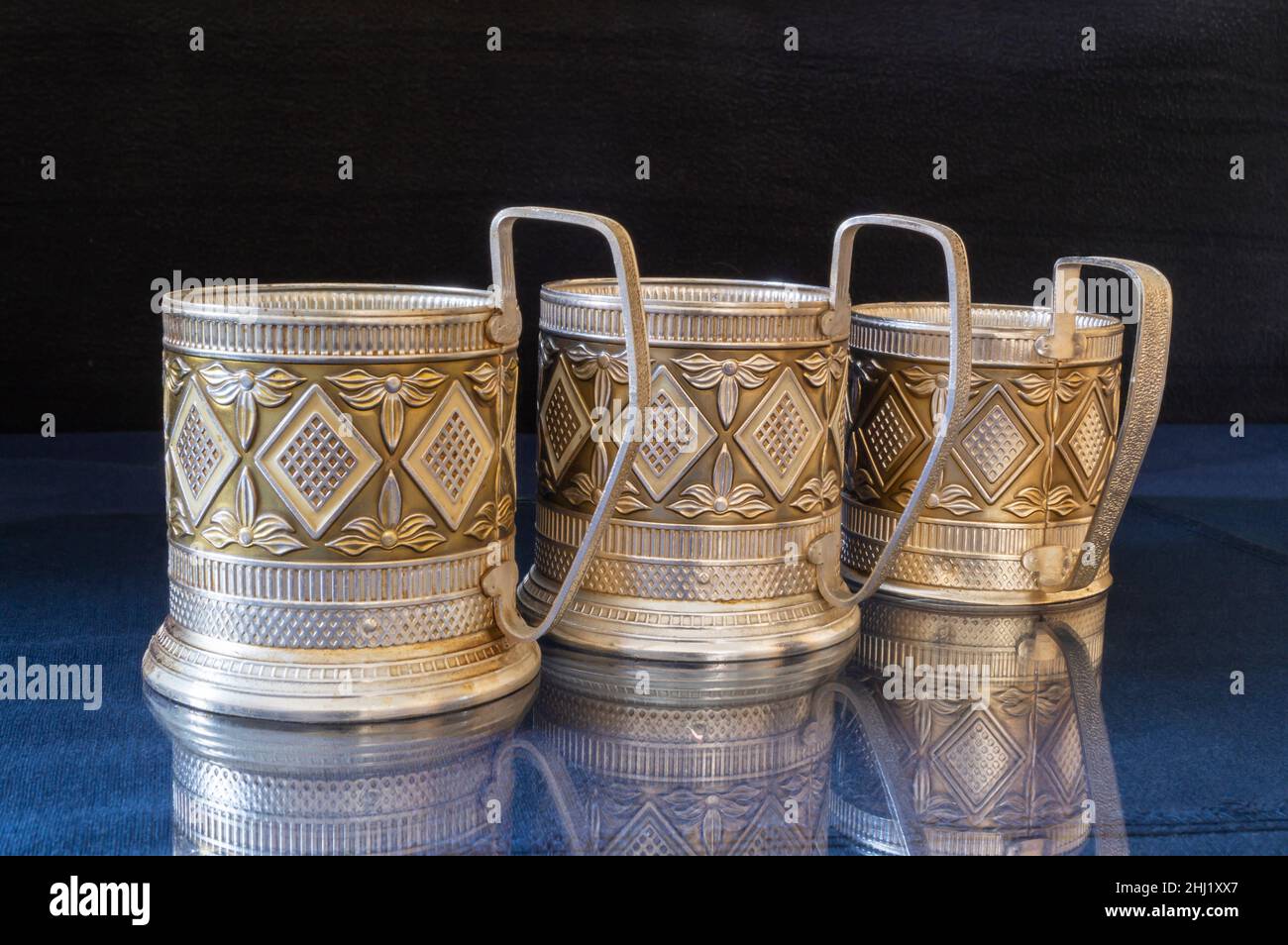 A metal cup holder on a blue table with a reflection. Kitchen utensils on a black background Stock Photo