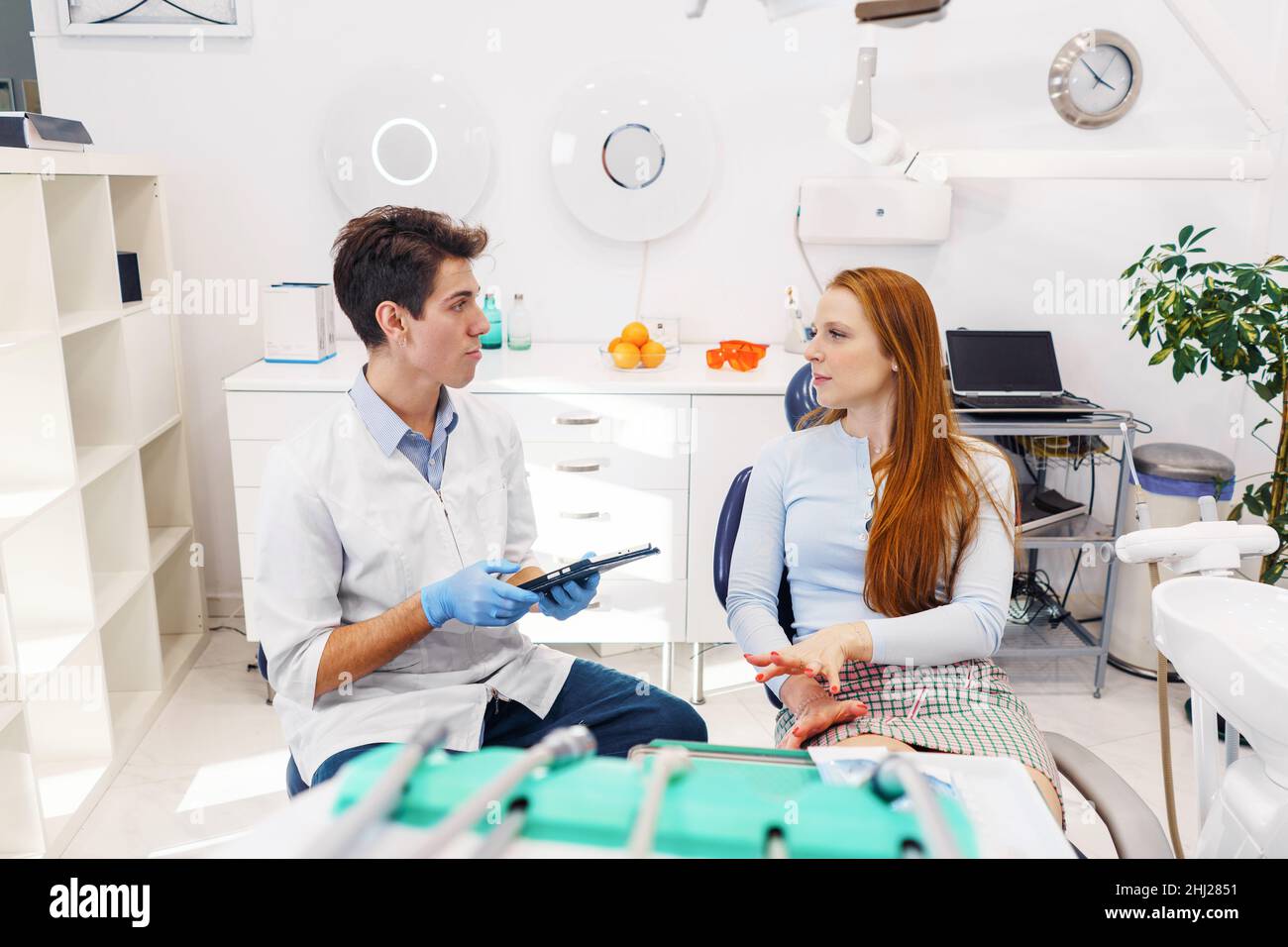 Male dentist with tablet and woman with long red hair looking at each other and talking during appointment in modern dental clinic Stock Photo