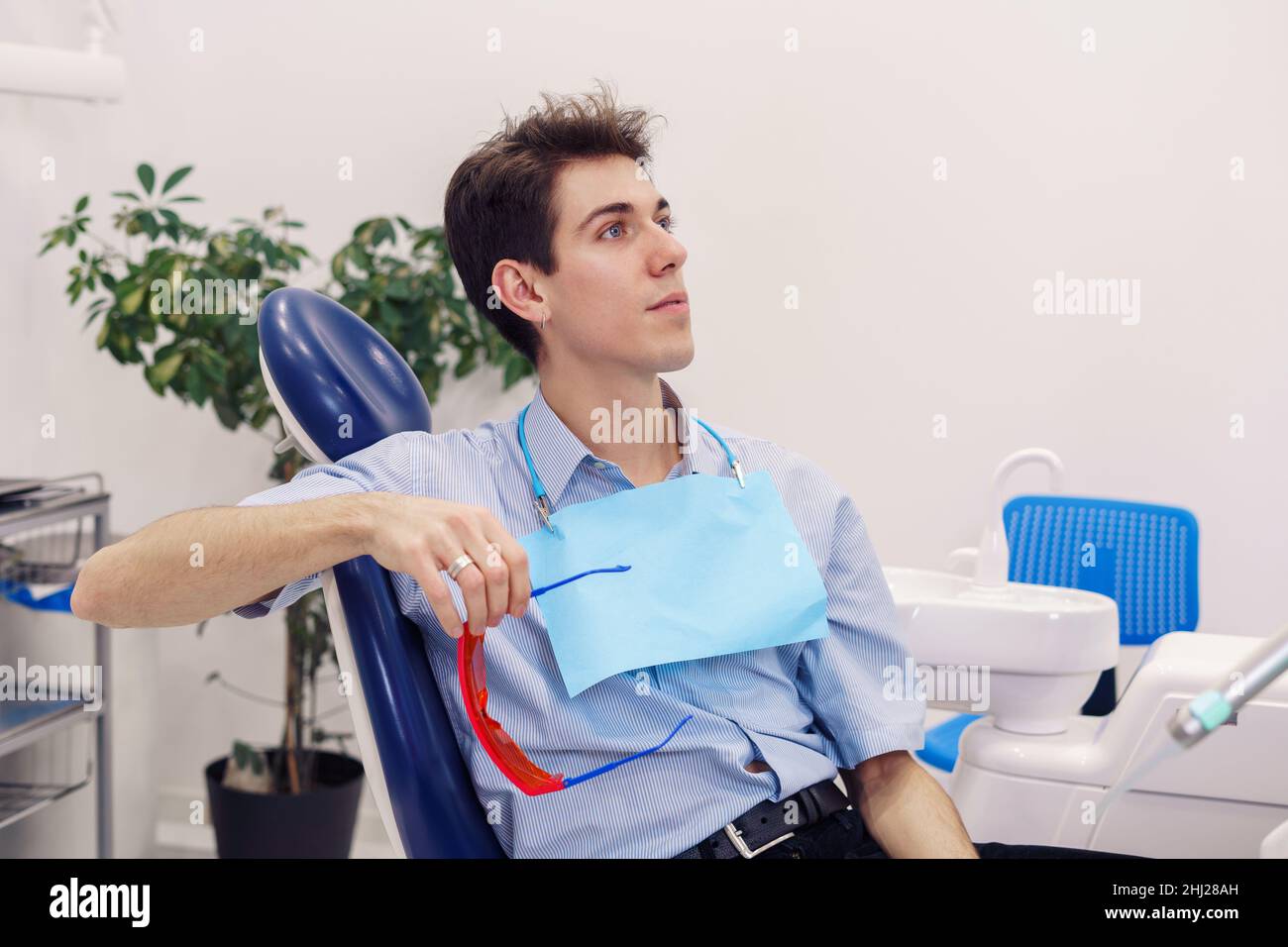 Young man with protective goggles looking away while sitting on chair in dentist office of modern clinic Stock Photo