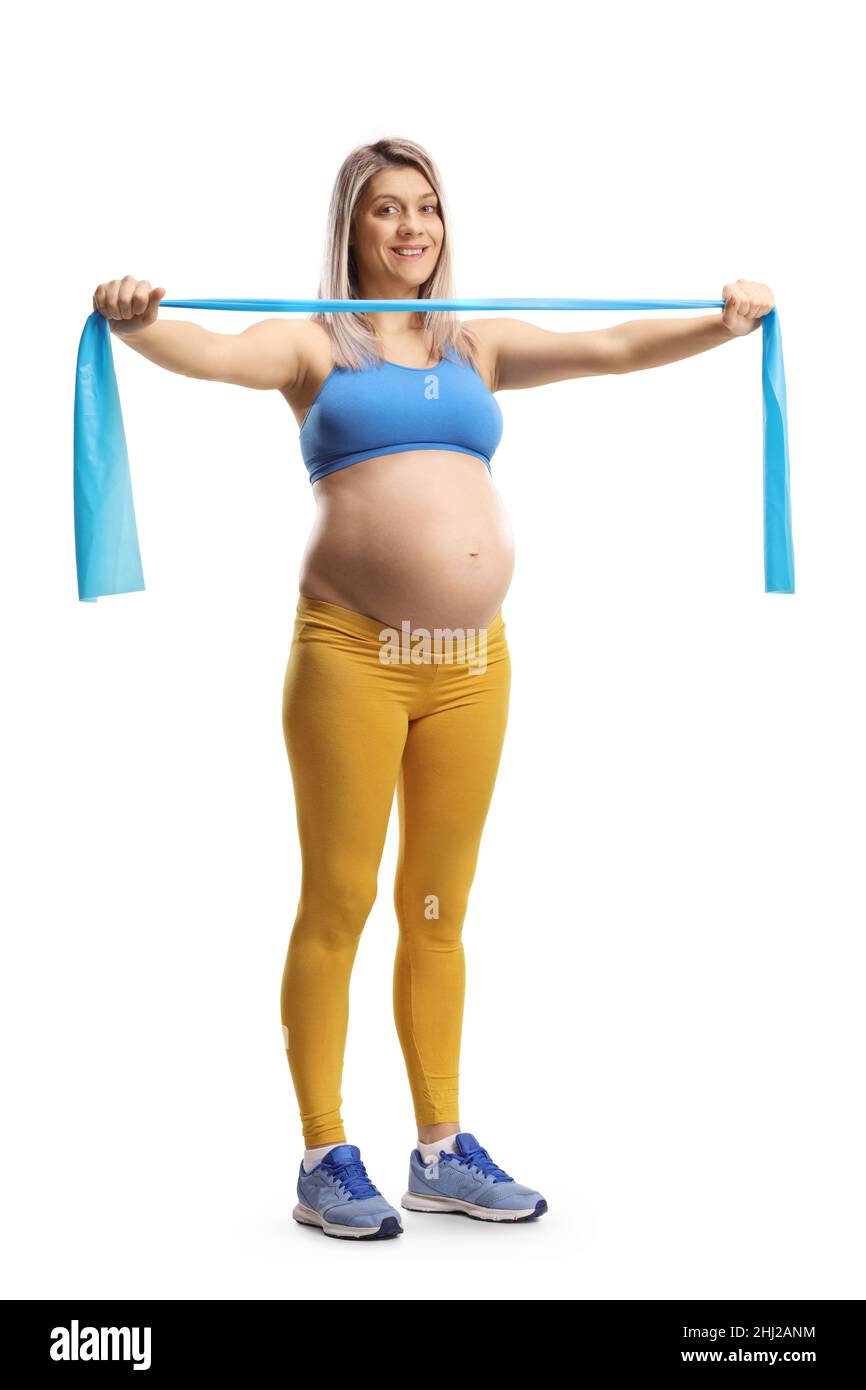 Full length portrait of a young pregnant woman in a crop top and leggings exercising with a stretch band isolated on white background Stock Photo